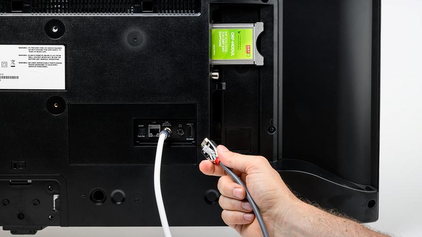 Ein ORF-Modul ist in den Modulschacht auf der Rückseite eines TV-Geräts gesteckt. Ein SAT-Kabel ist bereit angeschlossen. Ein HDMI-Kabel wird abgesteckt.