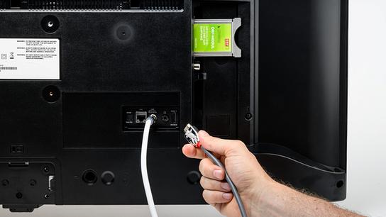 Ein ORF-Modul ist in den Modulschacht auf der Rückseite eines TV-Geräts gesteckt. Ein SAT-Kabel ist bereit angeschlossen. Ein HDMI-Kabel wird abgesteckt.